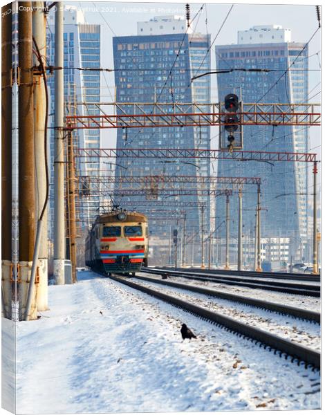 An electric train moves on rails against the backdrop of a cityscape of skyscrapers in a winter haze. Canvas Print by Sergii Petruk