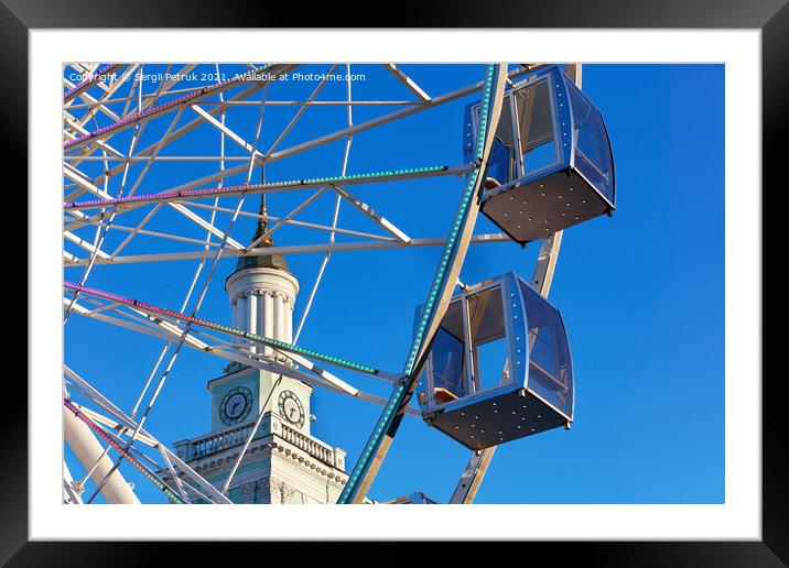 Empty cabins of the city's ferris wheel against the background of the blue sky and the spire of the old tower. Framed Mounted Print by Sergii Petruk
