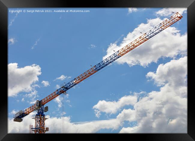 An arrow of a tower crane against a blue sky, divides the image diagonally. Framed Print by Sergii Petruk