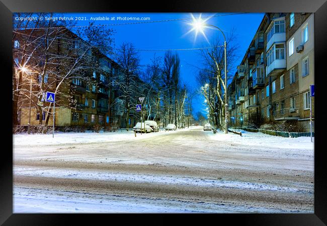 Snow-covered intersection on the road along a city street with trees in the snow and evening city illumination against the background of blue twilight. Framed Print by Sergii Petruk
