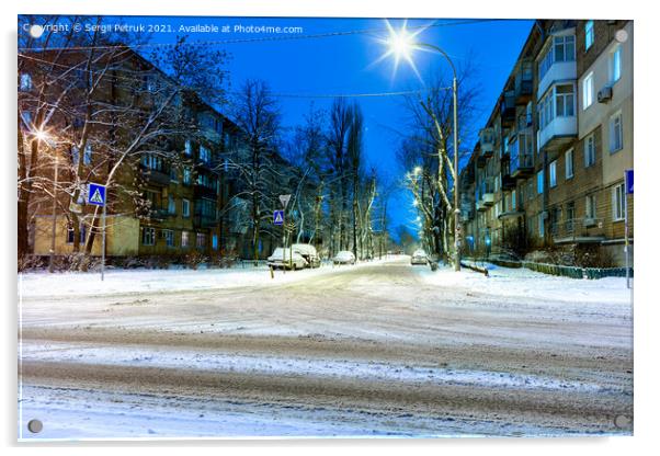 Snow-covered intersection on the road along a city street with trees in the snow and evening city illumination against the background of blue twilight. Acrylic by Sergii Petruk