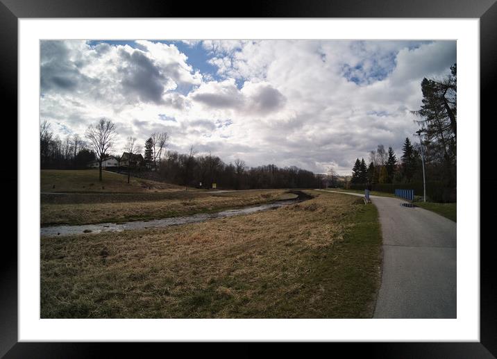 South Poland: Scenic view of at country side suburbs. View offers green grass in the summer and a gravel road that turns of along the river against dramatic clouds. Adventure and travel back in time. Framed Mounted Print by Arpan Bhatia