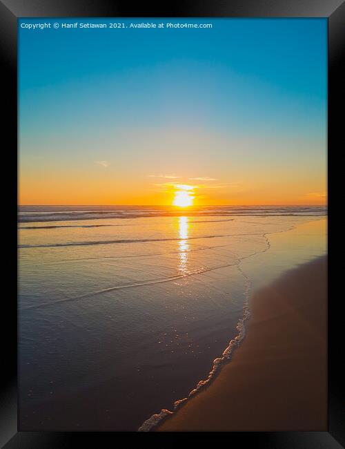 Wide sand beach reflecting orange sunset sunlight. Framed Print by Hanif Setiawan