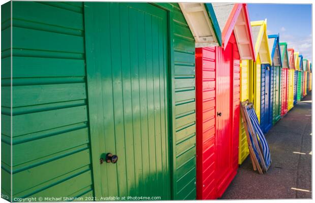Colourful Beach Huts and a deck chair in Whitby Canvas Print by Michael Shannon