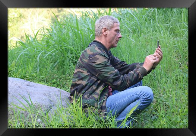 A Caucasian senior man using his phone in a meadow Framed Print by Hanif Setiawan