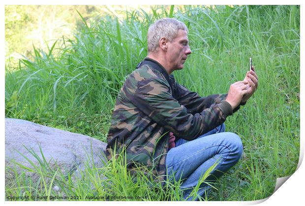 A Caucasian senior man using his phone in a meadow Print by Hanif Setiawan