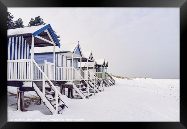 Beach huts covered in snow at low tide. Wells-next-the-sea, Norf Framed Print by Liam Grant