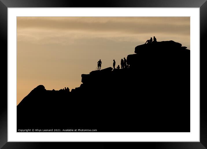 Silhouette of lots of people watching a climber at the summit of stanage edge. Climber wears a harness with tools like nuts, ropes and carabiners. Framed Mounted Print by Rhys Leonard