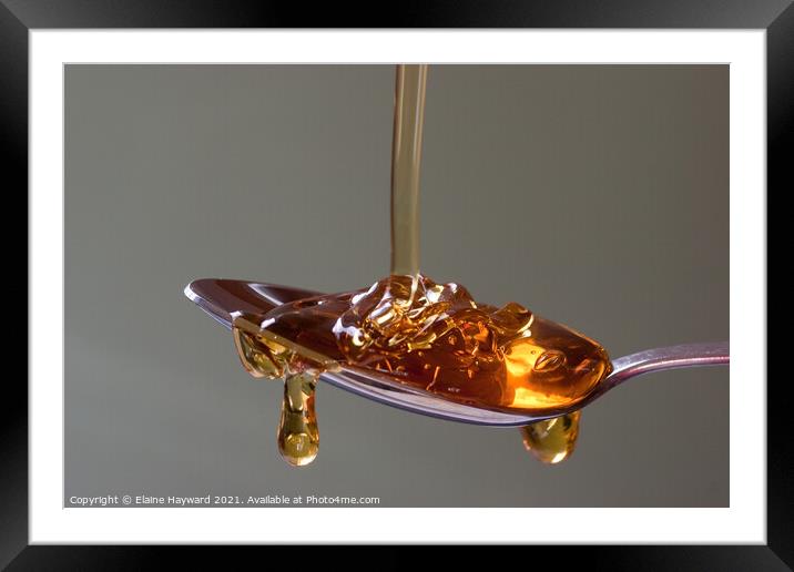Golden syrup dripping from a silver spoon Framed Mounted Print by Elaine Hayward
