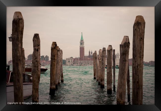 Wooden pillars at Venice bay symmetrically aligned pointing at Italian buildings in the back  Framed Print by Mihajlo Madzarevic