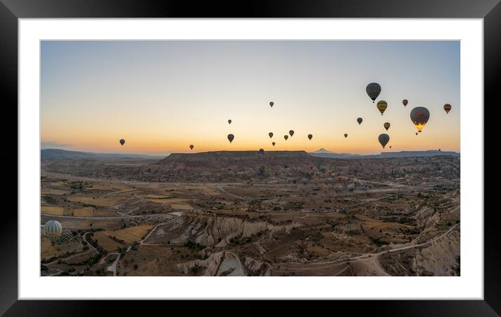 Cappadocia, Turkey - September 14, 2021: Wide angle Panorama aerial shot of colorful hot air balloons together floating in the sky at early morning in Goreme against volcanic hills Framed Mounted Print by Arpan Bhatia