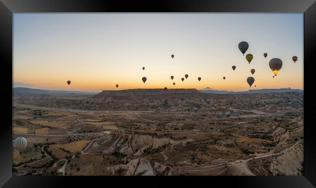 Cappadocia, Turkey - September 14, 2021: Wide angle Panorama aerial shot of colorful hot air balloons together floating in the sky at early morning in Goreme against volcanic hills Framed Print by Arpan Bhatia