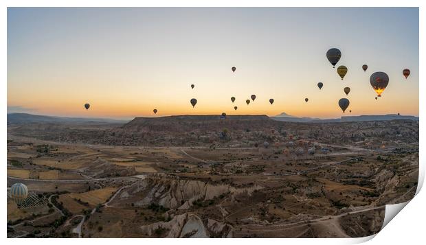 Cappadocia, Turkey - September 14, 2021: Wide angle Panorama aerial shot of colorful hot air balloons together floating in the sky at early morning in Goreme against volcanic hills Print by Arpan Bhatia