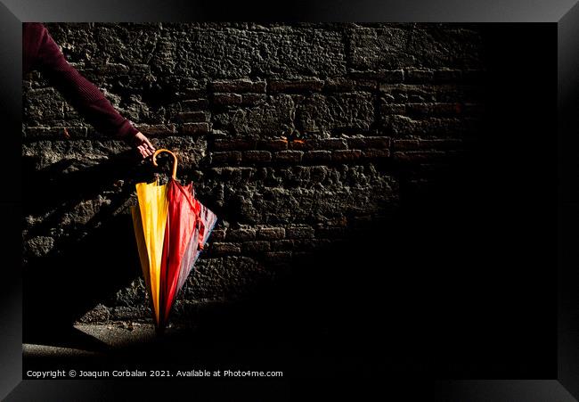A beautiful colored umbrella rests folded against a brick wall i Framed Print by Joaquin Corbalan