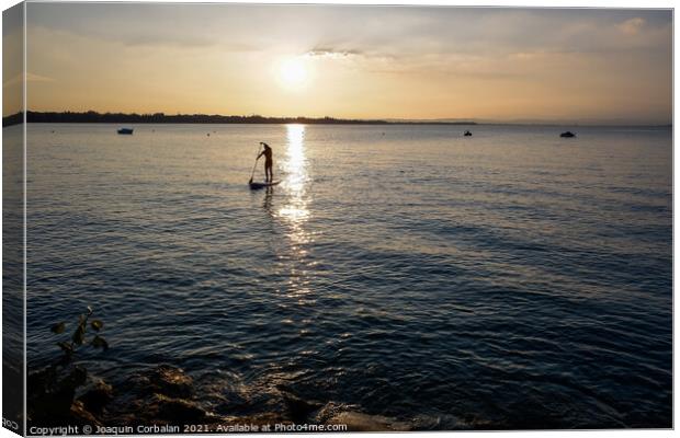 A young man on a paddle surf board approaches the shore of the l Canvas Print by Joaquin Corbalan