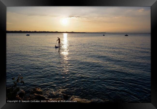 A young man on a paddle surf board approaches the shore of the l Framed Print by Joaquin Corbalan
