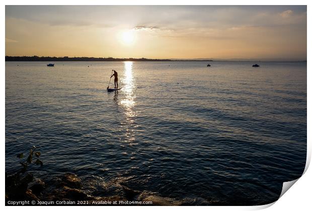 A young man on a paddle surf board approaches the shore of the l Print by Joaquin Corbalan
