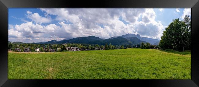 Panoramic view of green grass meadow countryside field with A shaped houses against sleeping knight tatra mountain aka as giewont and dramatic clouds located in Zakopane, South Poland, Europe Framed Print by Arpan Bhatia