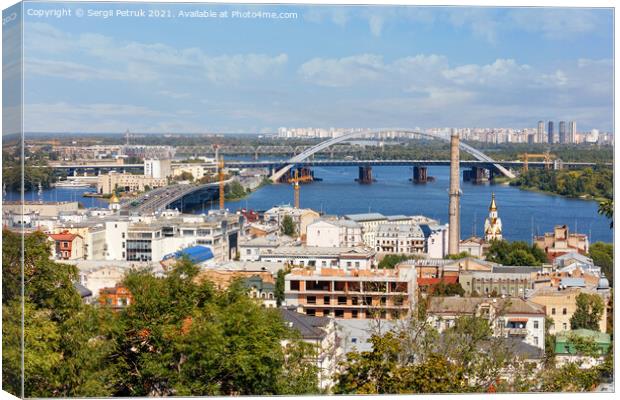 The landscape of summer Kyiv with a view of the old district of Podil with road and railway bridges, a chimney of an old boiler room and a bell tower with a gilded dome, the Dnipro River and many city buildings. Canvas Print by Sergii Petruk