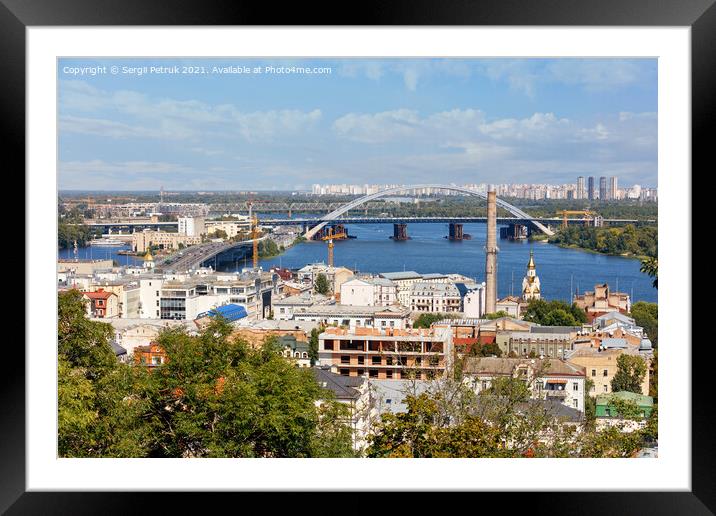 The landscape of summer Kyiv with a view of the old district of Podil with road and railway bridges, a chimney of an old boiler room and a bell tower with a gilded dome, the Dnipro River and many city buildings. Framed Mounted Print by Sergii Petruk