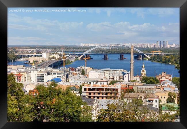 The landscape of summer Kyiv with a view of the old district of Podil with road and railway bridges, a chimney of an old boiler room and a bell tower with a gilded dome, the Dnipro River and many city buildings. Framed Print by Sergii Petruk
