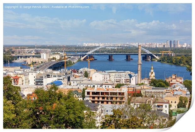 The landscape of summer Kyiv with a view of the old district of Podil with road and railway bridges, a chimney of an old boiler room and a bell tower with a gilded dome, the Dnipro River and many city buildings. Print by Sergii Petruk