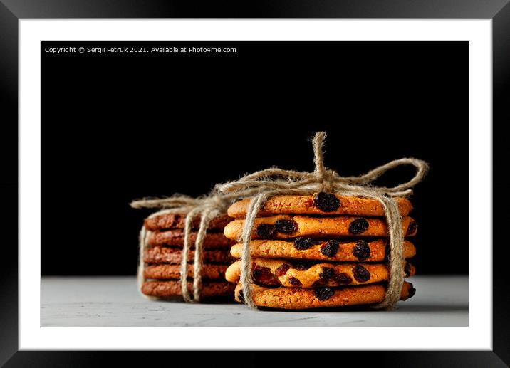 Stacks of homemade oatmeal and chocolate biscuits tied with a rope lie on a gray concrete surface against a black background. Close-up, copy space. Framed Mounted Print by Sergii Petruk