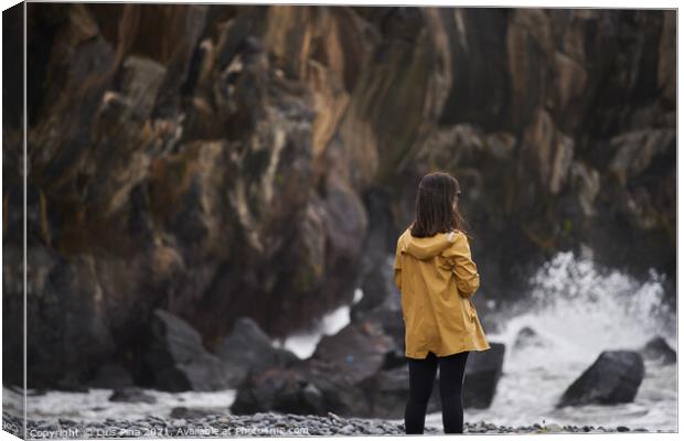Woman on a yellow rain jacket looking to the sea with rocks on the background, in Madeira Canvas Print by Luis Pina