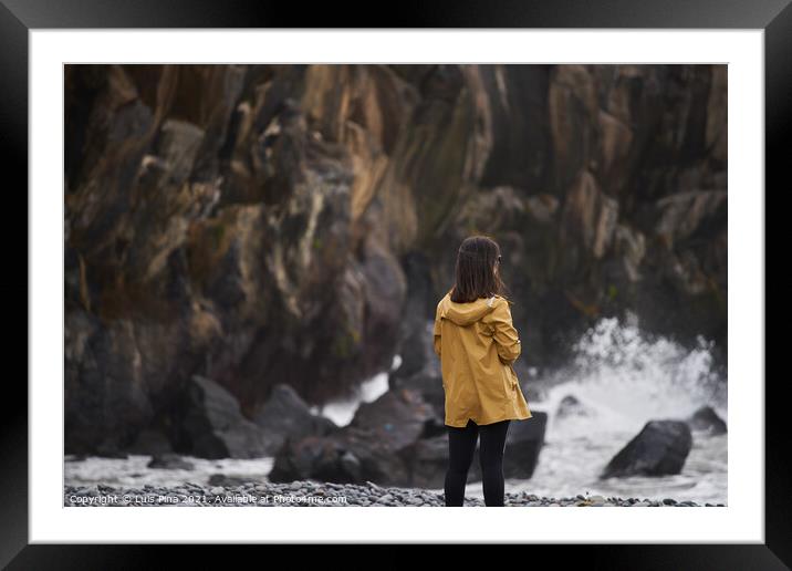 Woman on a yellow rain jacket looking to the sea with rocks on the background, in Madeira Framed Mounted Print by Luis Pina