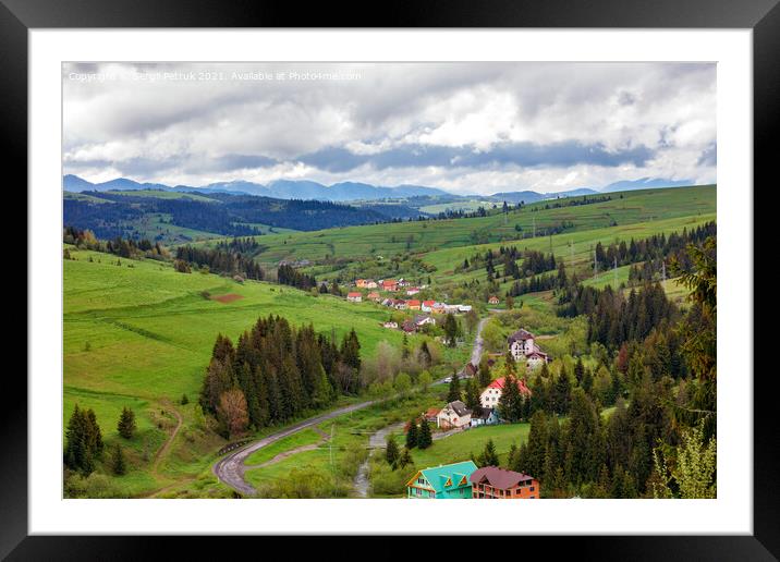 A picturesque landscape of a Carpathian village with a winding road and colorful roofs in early spring. Framed Mounted Print by Sergii Petruk