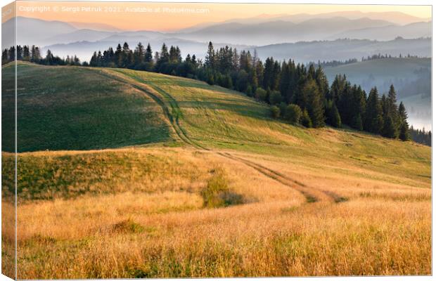 Morning landscapes of the mountainous Carpathians, sunrise illuminates the rural road that runs along the ridge of the hill. Canvas Print by Sergii Petruk
