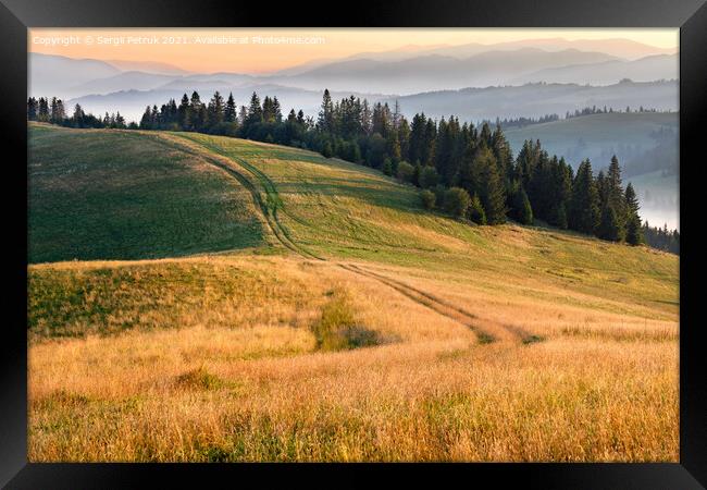 Morning landscapes of the mountainous Carpathians, sunrise illuminates the rural road that runs along the ridge of the hill. Framed Print by Sergii Petruk