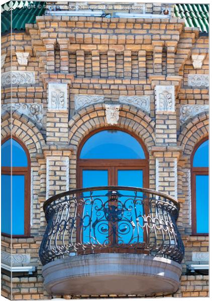 Arched windows with a beautiful, expressive balcony on the brick facade of the old house and the reflection of the blue sky in the glass windows. Canvas Print by Sergii Petruk