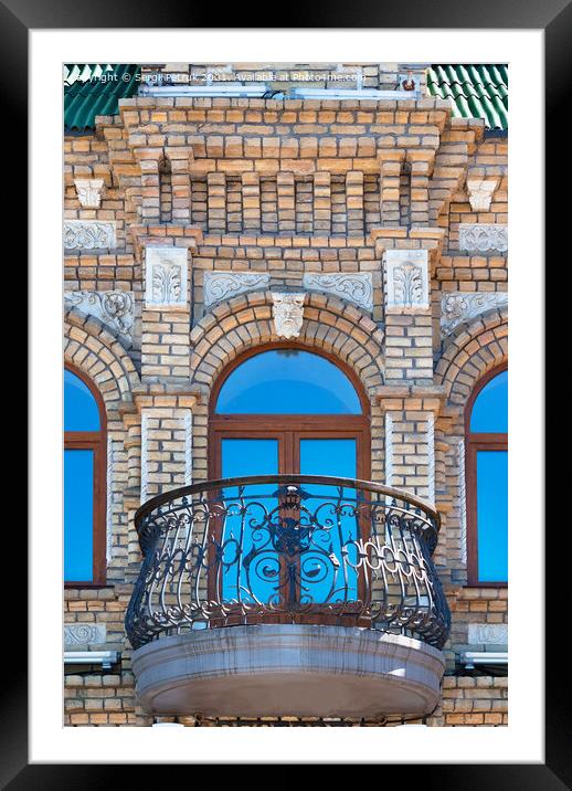 Arched windows with a beautiful, expressive balcony on the brick facade of the old house and the reflection of the blue sky in the glass windows. Framed Mounted Print by Sergii Petruk