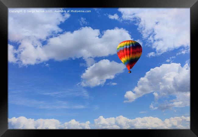 A motley multicolored hot air balloon raises a basket with tourists in the blue sky among white clouds. Framed Print by Sergii Petruk