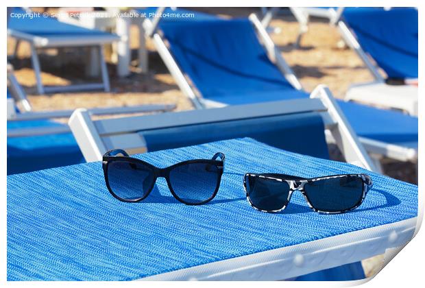 A pair of sunglasses lie on a blue sun lounger under the sun on a summer day. Print by Sergii Petruk