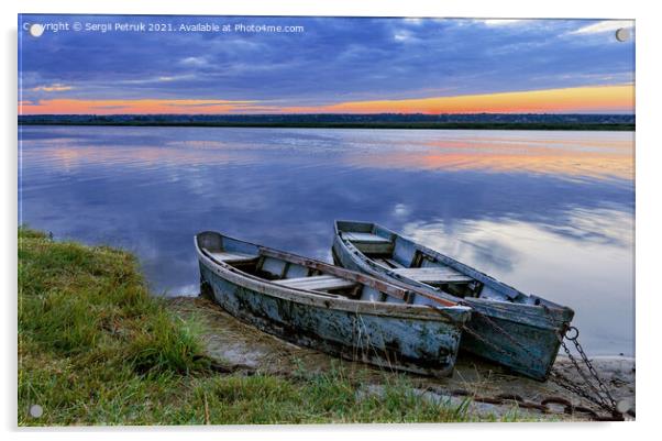 Two old dilapidated boats are moored with a metal chain to the bank of a calm river in the early morning against the backdrop of a cloudy sky and the rising sun. Acrylic by Sergii Petruk