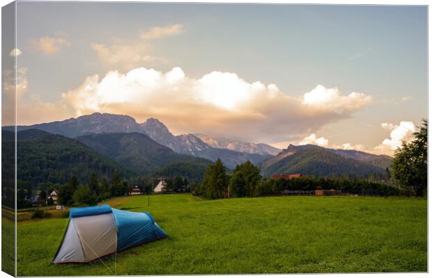 Camping tent put up on green grass meadow field against tatra mountains landscape during sunset sunrise and dramatic clouds, adventure in wild nature concept. Canvas Print by Arpan Bhatia