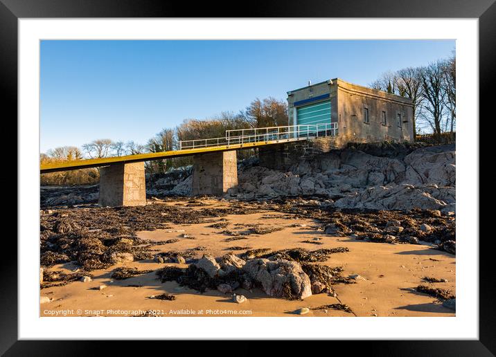 A coastal boat house and boat launch ramp slipway on a rocky beach in winter Framed Mounted Print by SnapT Photography