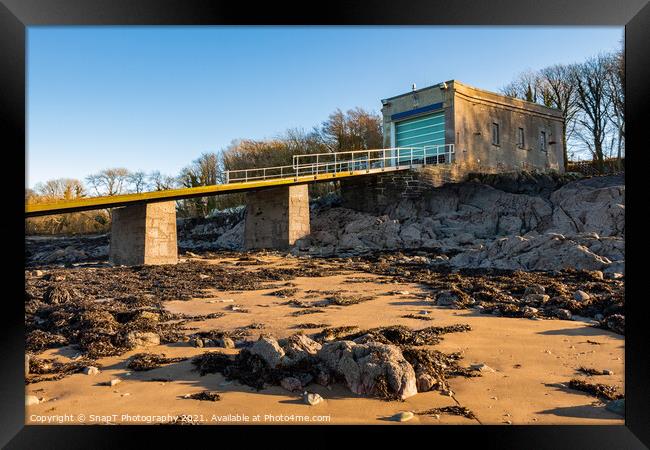 A coastal boat house and boat launch ramp slipway on a rocky beach in winter Framed Print by SnapT Photography