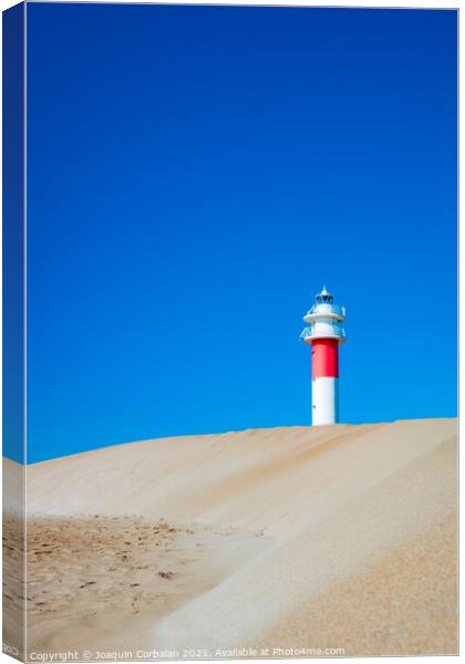 A lighthouse seen from the sand dunes of a beach on a sunny day. Canvas Print by Joaquin Corbalan