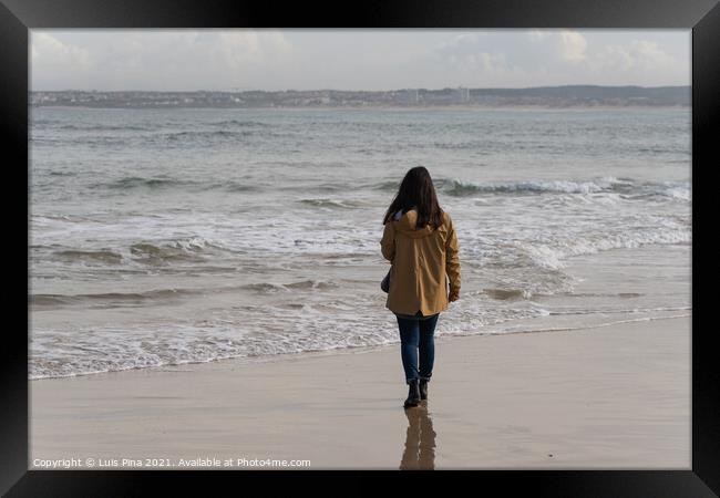 Woman walking on a beach with a yellow jacket in Peniche, Portugal Framed Print by Luis Pina