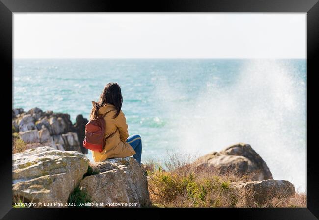 Caucasian traveler woman looking at the waves on the sea with a yellow jacket in Peniche, Portugal Framed Print by Luis Pina