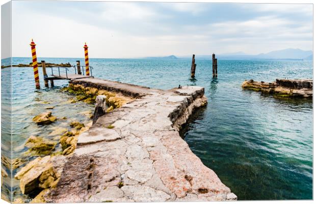 Old stone jetty at the tip of San Vigilio, on Lago di Garda with colorful mooring poles on Canvas Print by Joaquin Corbalan