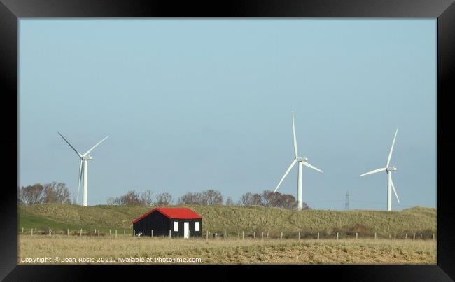 Black hut with red roof and wind turbines at Rye Harbour Framed Print by Joan Rosie
