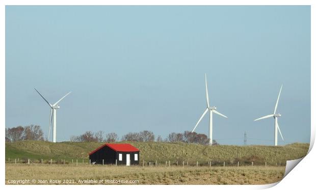 Black hut with red roof and wind turbines at Rye Harbour Print by Joan Rosie