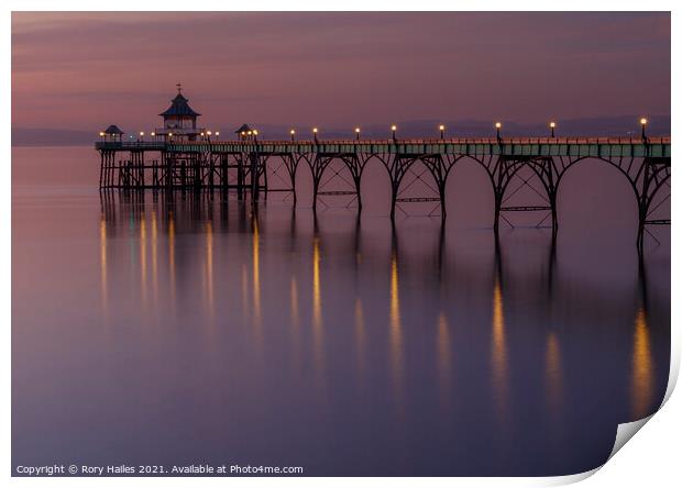 Clevedon Pier with lights reflecting onto a calm sea Print by Rory Hailes