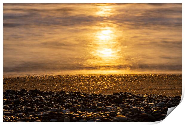Golden sunlight on sea and pebble beach Print by Phil Crean