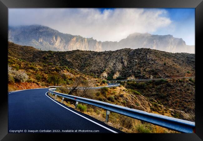 Winding road leads to high mountains with clouds to escape the r Framed Print by Joaquin Corbalan