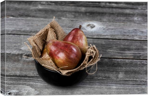 Raw whole pears inside of bowl on aged wooden table in close up  Canvas Print by Thomas Baker